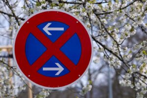 Blue and red no parking sign surrounded by white spring blossoms on trees.