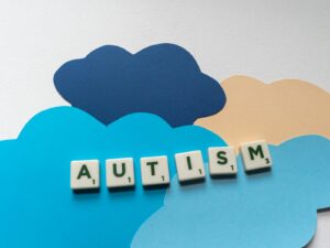 Scrabble tiles spelling 'Autism' on colorful paper clouds, promoting autism awareness creatively.