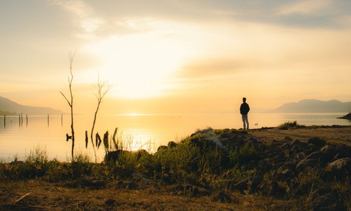 Serene silhouette of a man admiring the sunset at Lake Chapala shoreline in Jocotepec, Mexico.
