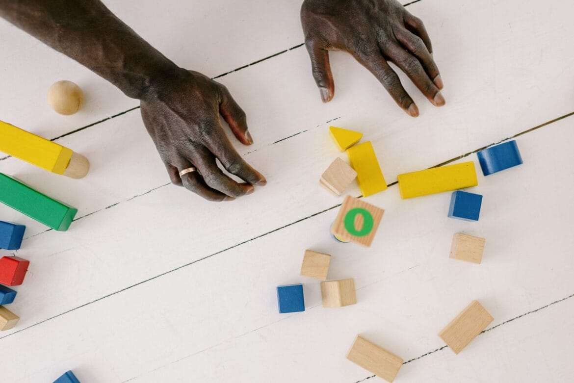 Hands playing with colorful wooden blocks on a white table, sparking creativity and learning.