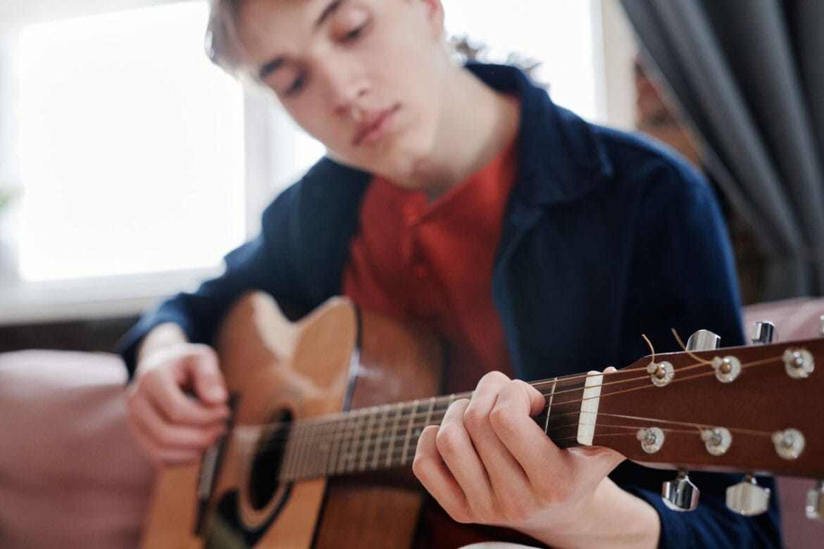 Young man sitting indoors playing an acoustic guitar with focus on talent and music.